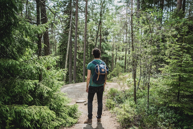 Ein Mann mit Rucksack steht an einer Lichtung mittem im grünen Wald.